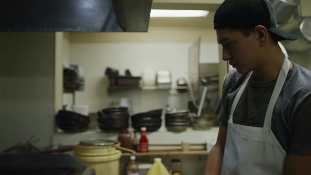 十几岁的西班牙裔男性厨师戴上橡胶手套，用水壶在墨西哥餐馆的商用煎锅上涂油视频素材