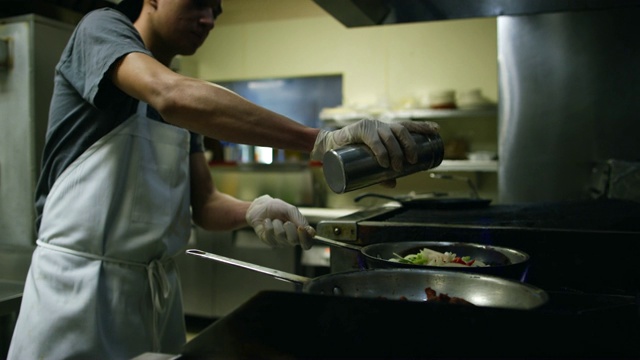 十几岁的墨西哥厨师在一个墨西哥餐馆的商业范围里用两个平底锅给肉和蔬菜调味视频下载