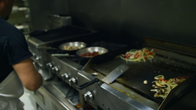 墨西哥餐馆里，三十多岁的西班牙男厨师在煎锅上搅拌蔬菜前撒调料视频素材