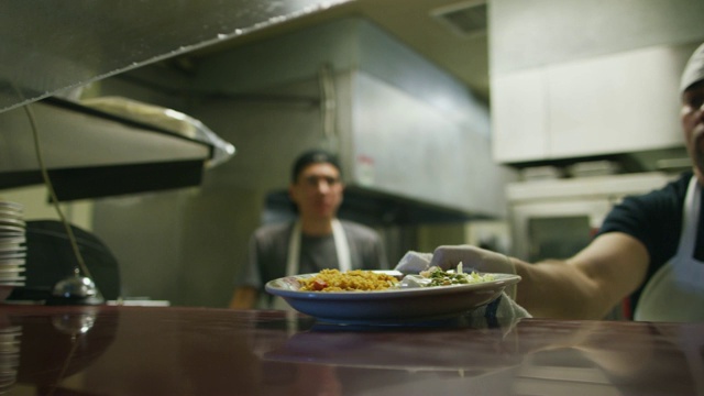 年轻的墨西哥男厨师在一家餐厅，将蒸盘子和法士塔斯放在窗口，摇铃让服务员拿起视频素材
