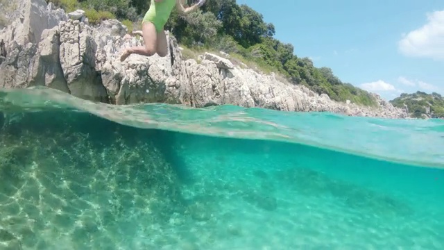 一名少女从岩石上跳到阳光明媚的蓝绿色海洋中，克罗地亚，佩莱沙茨视频素材