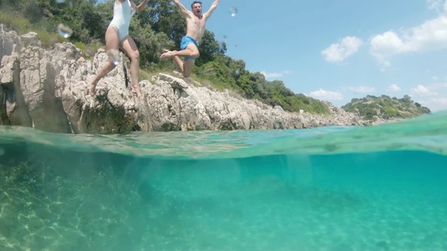 克罗地亚Peljesac，一对夫妇从岩石上跳到阳光明媚的蓝绿色海洋中视频素材