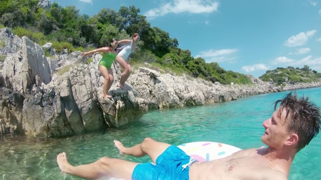 克罗地亚Peljesac，戴着充气戒指的父亲看着十几岁的女儿从岩石上跳入阳光明媚的海洋视频素材