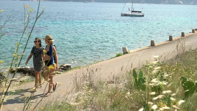 母女俩走在克罗地亚Peljesac阳光明媚的海滨木板路上视频素材