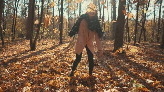 快乐的女孩正在从森林里的地上摘干枫叶，然后呕吐视频素材