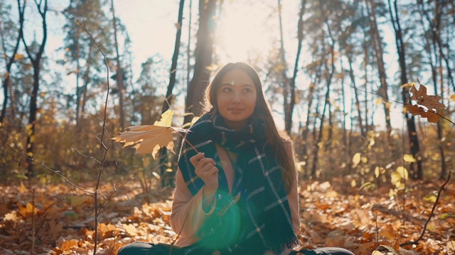 漂亮的女孩手里拿着枫叶玩，坐在秋天的森林里视频素材