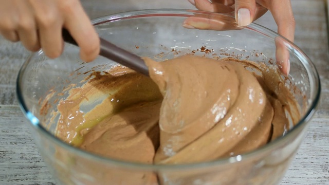 糕点师在煮生面团。在烤巧克力饼干蛋糕时，一只手用塑料抹刀在一个玻璃碗里搅拌面团。视频素材