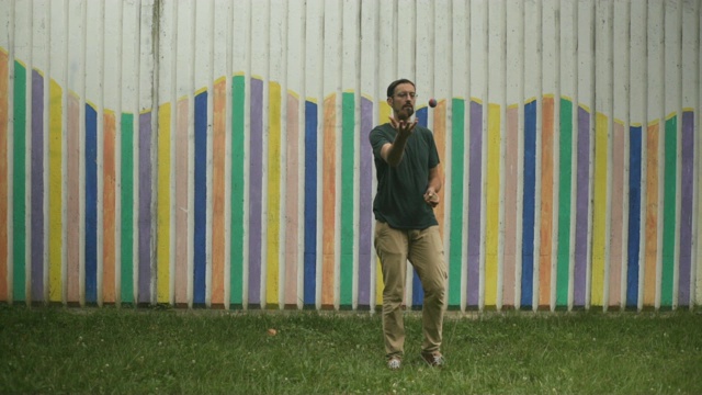 男子艺人的手和腿显示杂耍球，杂耍，慢动作，彩色墙壁的背景。视频下载
