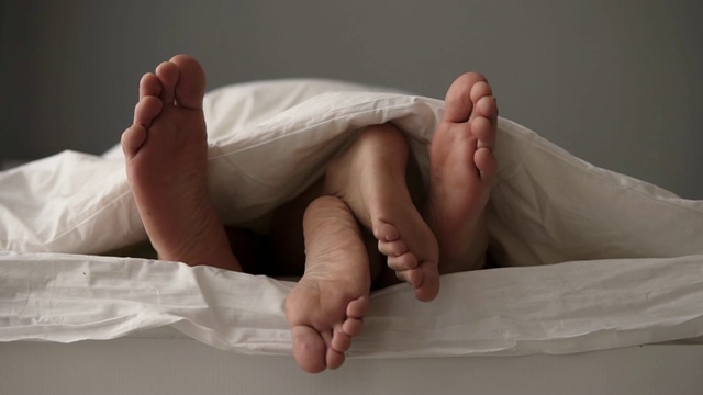 年轻美丽和相爱的夫妇躺在床上的特写。他们的脚在毯子下面，而早上醒来在床上。女人躺在男人身上，她的脚在男人之间视频素材