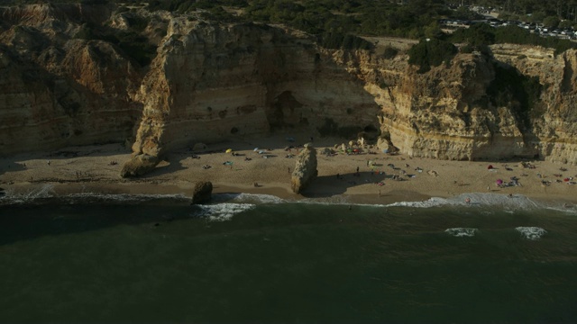 鸟瞰图，人们放松附近的悬崖在马里亚海滩/马里亚海滩，法罗，葡萄牙视频下载