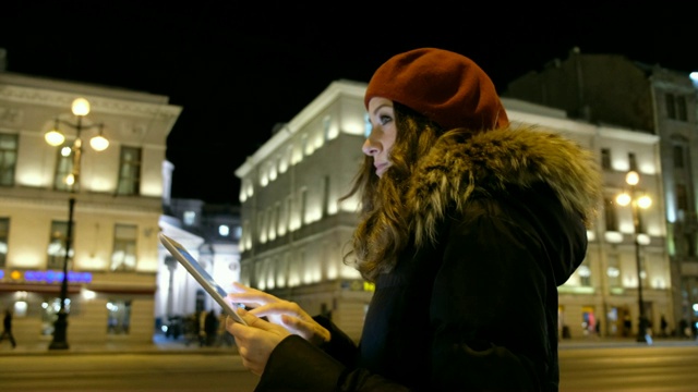 迷人的女孩看着平板电脑和等待公共汽车在晚上在城市。视频素材