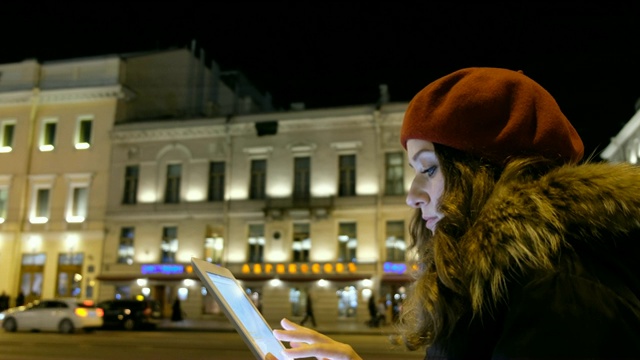 迷人的女孩看着平板电脑和等待公共汽车在晚上在城市。视频素材