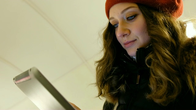 一个迷人的女孩的特写，手拿着平板电脑在地铁的自动扶梯上，看着触摸屏，在屏幕上移动你的手指视频素材