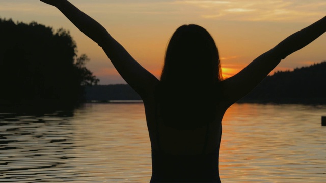 快乐的女人在日落湖举起她的手臂和转身视频素材