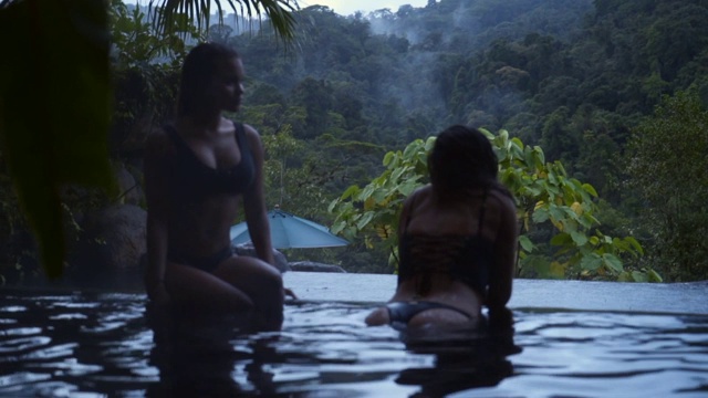 慢镜头:两个穿着比基尼的年轻女子从游泳池看丛林视频素材