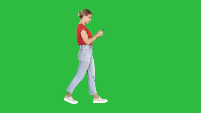 美丽的年轻女子走路和阅读短信在她的手机上的绿色屏幕，色度键视频素材
