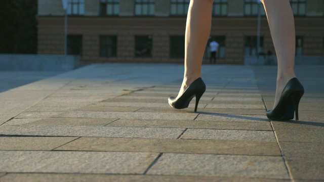 女人们穿着高跟鞋走在城市的街道上。穿着高跟鞋的年轻女商人的脚在城市中穿行。女孩走着去上班。慢动作近景低角度视图视频素材