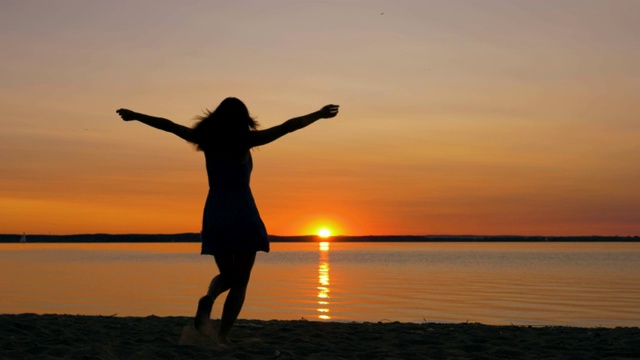 一个女人跑向海滩上的日落，举起她的手，转身视频素材