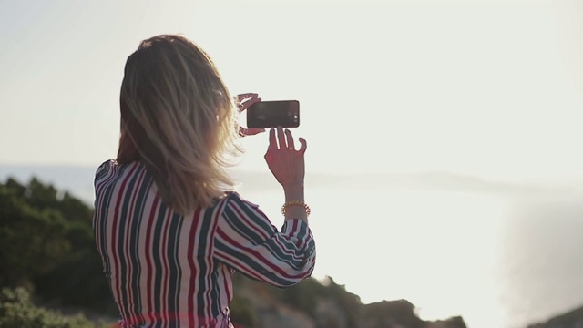 旅行者女孩的后视图停留在巨大的岩石前面的深蓝色看到和用她的智能手机拍照。视频素材