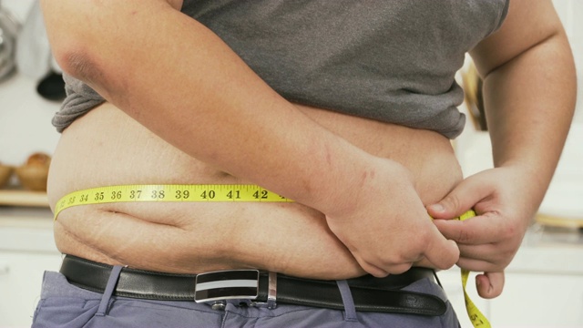 特写正面视图:超重男子测量他的腹部与卷尺英寸视频下载