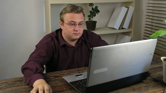 疲惫的戴着眼镜的商人在办公室里靠近笔记本电脑。视频素材