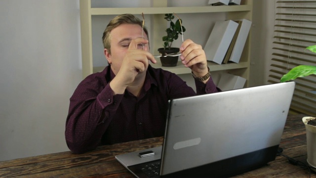 疲惫的戴着眼镜的商人在办公室里靠近笔记本电脑。视频素材