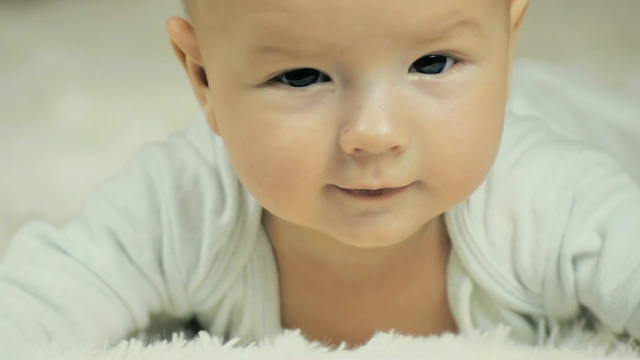一个六个月大的男孩躺在地上看着镜头，微笑着用慢动作拍摄。视频素材