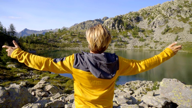 年轻男子徒步旅行在夏天通过惊人的高山湖泊手臂伸出庆祝个人目标。年轻人张开双臂，站在大自然中视频素材