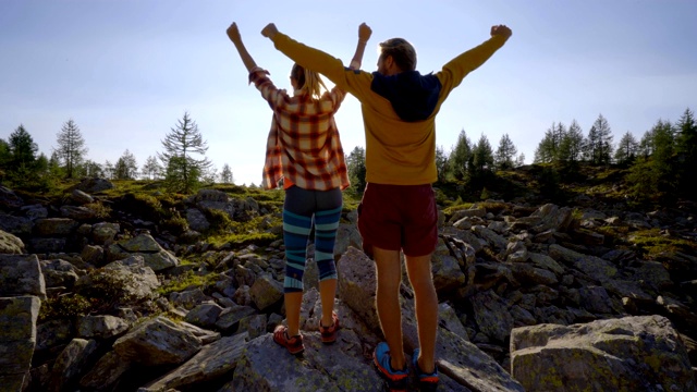 年轻的夫妇在徒步旅行的山峰周围，双臂张开在阳光下，夫妇徒步双臂张开自由和成就的概念视频素材