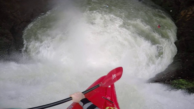 一个男人划着皮划艇沿着河上的瀑布而下。视频下载