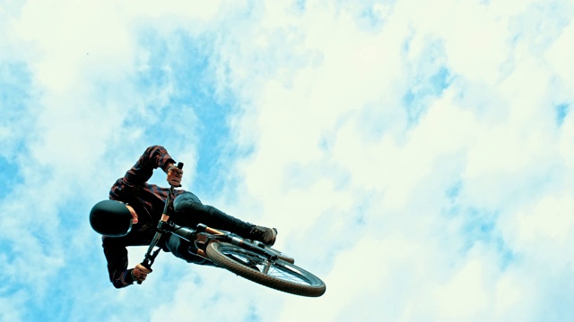 在蓝天白云的映衬下，年轻男子向后翻转BMX自行车视频素材