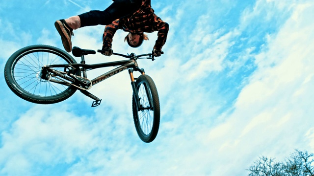年轻男子在多云的天空下跳跃和旋转BMX自行车视频素材