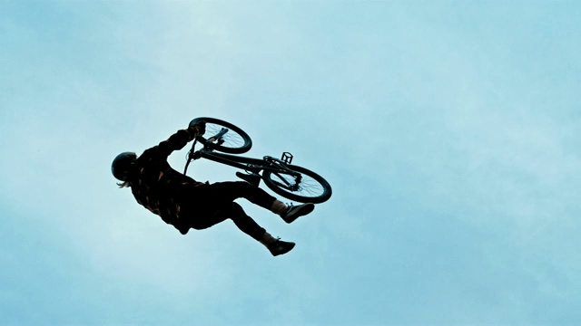 在蓝天的映衬下，年轻男子向后翻转BMX自行车视频素材