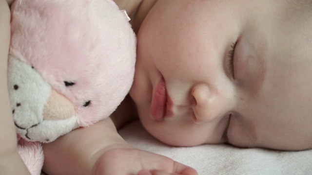 一个可爱的新生女孩和一个柔软的粉红色的猫玩具在甜蜜地睡觉的特写视频素材