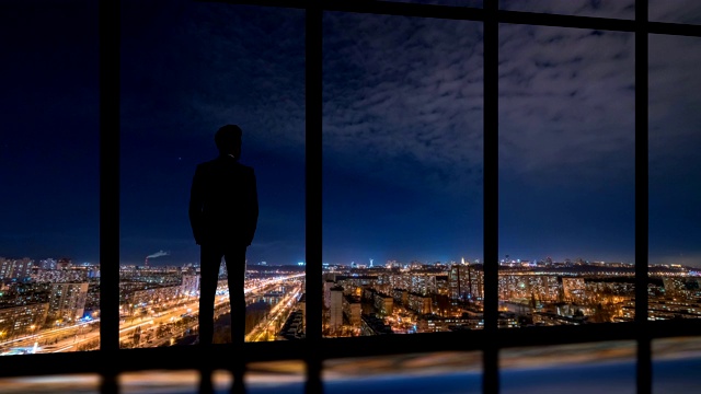 站在窗边的男子，夜色中的城市背景。时间流逝视频素材