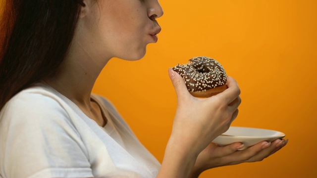 女孩咬巧克力甜甜圈，高热量的甜食，增加了血糖糖尿病视频素材