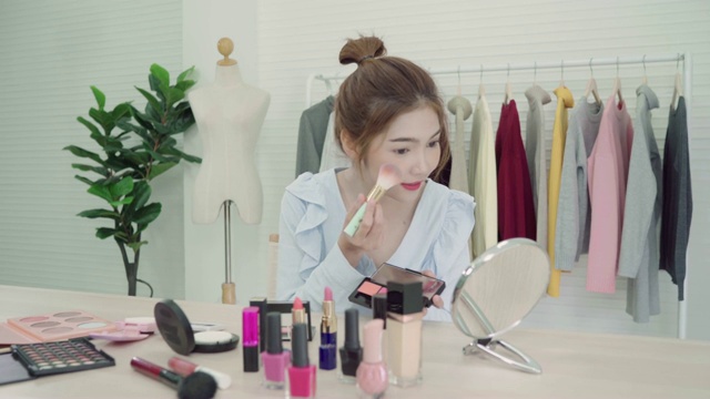 美妆博主坐在镜头前拍摄美妆视频。美丽的亚洲女性一边化妆一边复习化妆教程，由互联网在社交网络上直播。视频下载