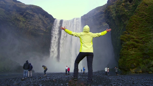 无忧无虑的女人张开双臂站在Skogafoss瀑布下视频素材