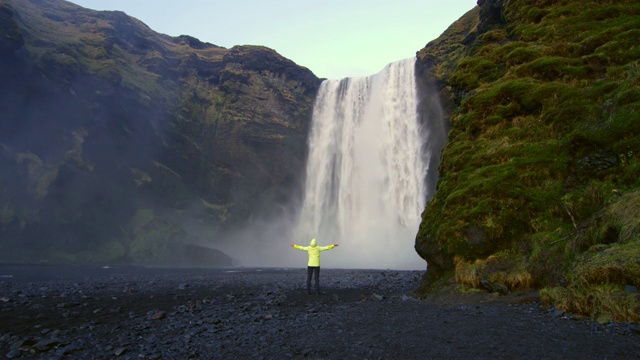 无忧无虑的女人伸出双臂站在斯科加佛瀑布下，冰岛视频素材