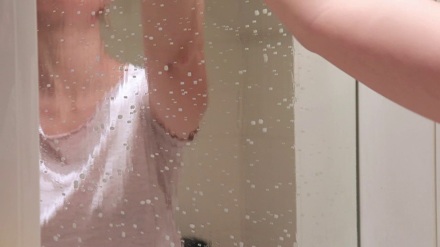 一个戴着黄色橡胶手套的不可辨认的女人正在用黄色的抹布和泡沫清洁剂清洗浴室的镜子。清洁、擦拭和清洗镜子的概念视频素材