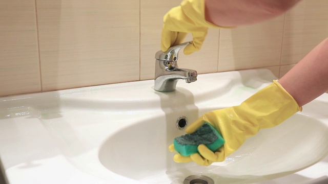 一个戴着黄色橡胶手套的不可辨认的女人正在浴室水槽里用水洗海绵。清洁和洗涤概念视频素材