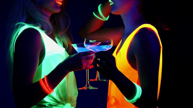 迷人的视频性感的网络raver女人拍摄在荧光衣服下的紫外线黑光。两个性感的网络发光raver女人拍摄在紫外线黑光下荧光衣服，派对概念视频下载