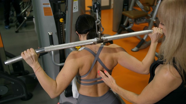 教练在健身房进行训练。背部的锻炼让一个漂亮的黑发女子4K慢动作视频下载