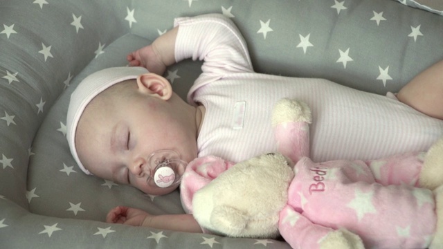 半岁的可爱小女孩穿着粉红色的衣服和一只粉红色的泰迪熊睡觉视频素材