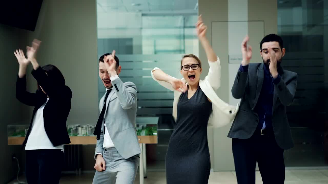 快乐的商务团队的男男女女在工作聚会上跳舞，一起移动身体，在大厅里放松地笑着唱着歌。同事、放松和情感观念。视频素材