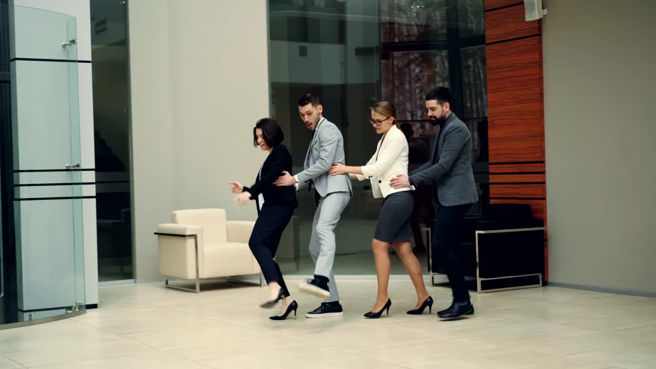 俏皮的同事们正穿着西装享受着工作派对，在大厅里跳舞，放松和欢笑。非正式沟通，快乐和团队概念。视频素材