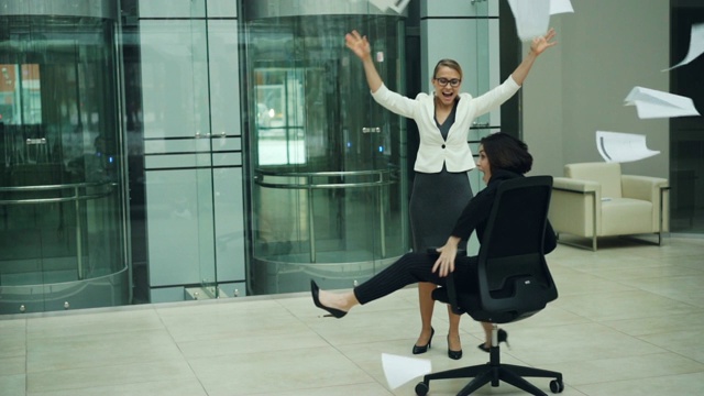 慢镜头中，欢快的年轻女性坐在办公室大厅的转椅上旋转，扔纸，然后大笑。工作场所的快乐概念。视频素材