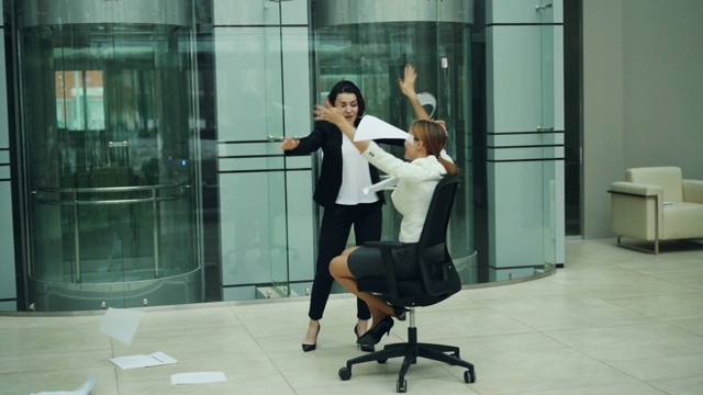 慢镜头中，兴奋的女商人们在转椅上旋转，把纸抛向空中，笑着玩。积极的情绪，工作和同事的概念。视频素材