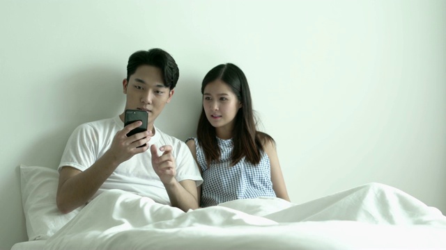 年轻情侣早上在床上用智能手机自拍。视频素材