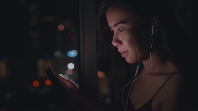 年轻的亚洲女性在晚上用手机听音乐视频下载